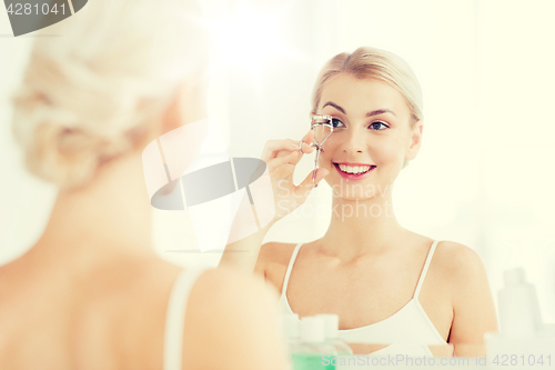 Image of woman with curler curling eyelashes at bathroom