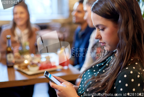 Image of woman with smartphone and friends at restaurant