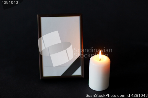 Image of black ribbon on photo frame and candle at funeral