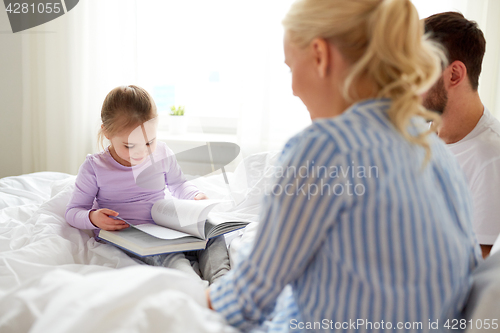 Image of happy family reading book in bed at home