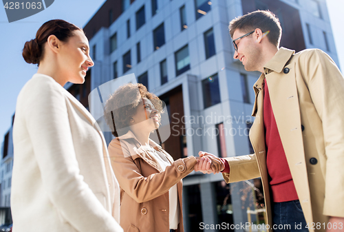 Image of happy people shaking hands on city street