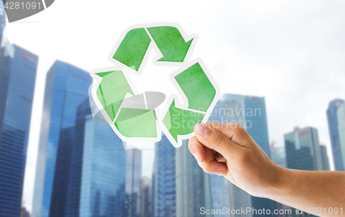 Image of close up of hand with green recycle sign in city