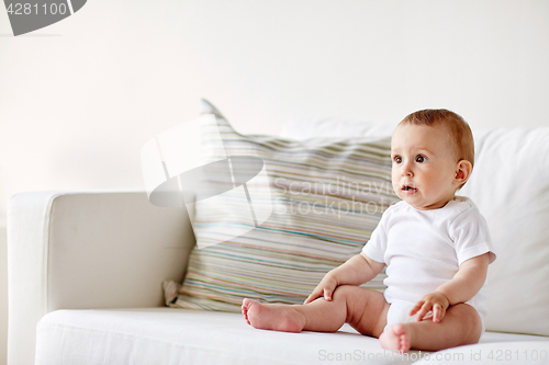 Image of happy baby boy or girl sitting on sofa at home