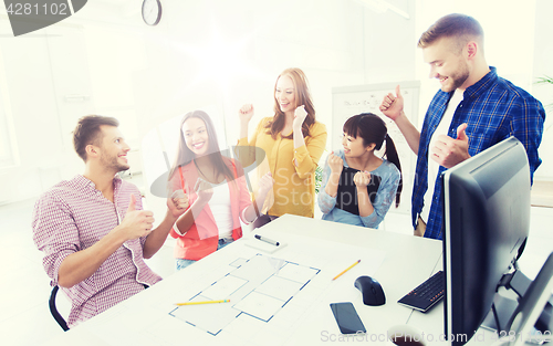 Image of happy creative team celebrating success at office