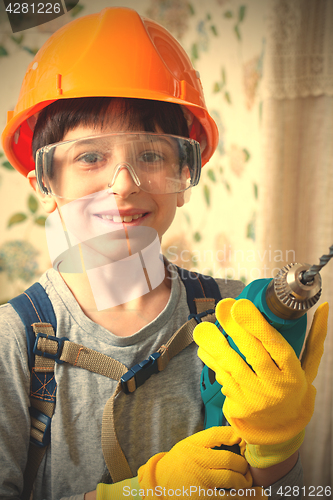 Image of boy in a construction helmet and safety goggles with a drill in 