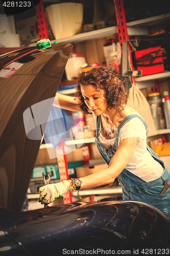 Image of woman mechanic with a wrench adjusts the car\'s engine