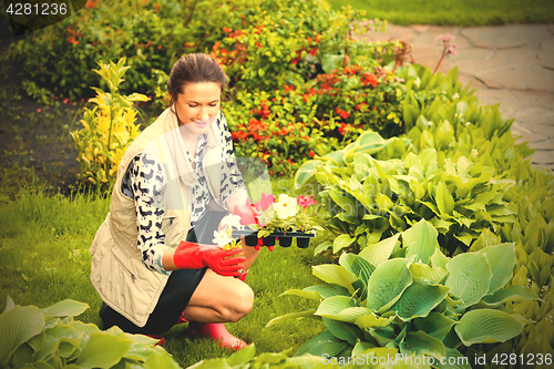 Image of smiling middle-aged woman in red rubber gloves planting flowers