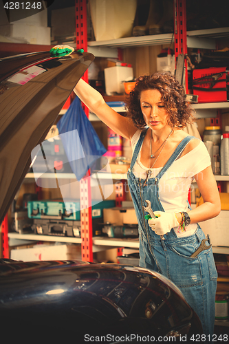 Image of beautiful woman in a jeans jumpsuit of a car mechanic opened the