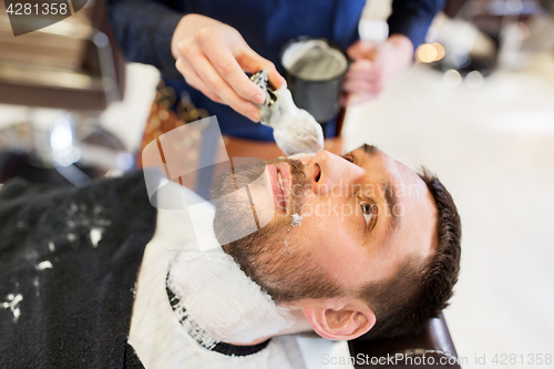 Image of man and barber applying shaving foam to beard