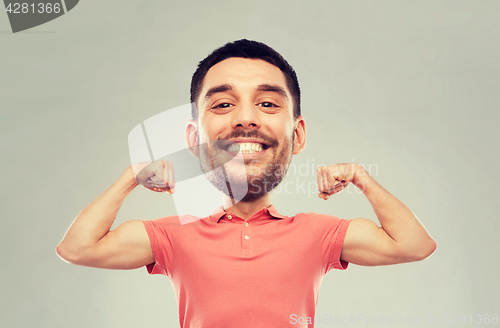 Image of smiling man showing biceps over gray background