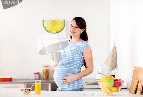 Image of happy pregnant woman with cup at home kitchen