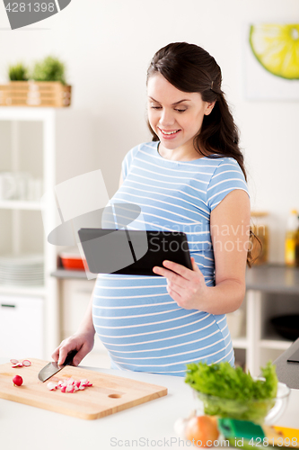 Image of pregnant woman with tablet pc cooking at home