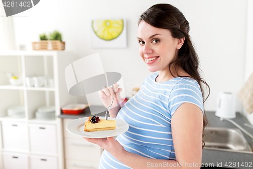 Image of happy pregnant woman eating cake at home kitchen