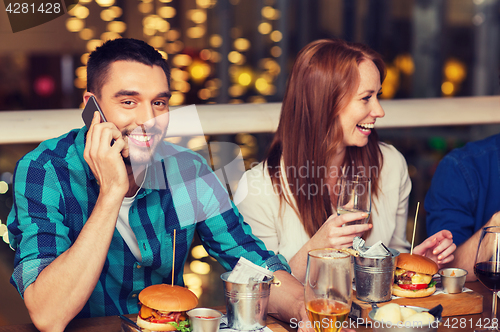 Image of man with smartphone and friends at restaurant