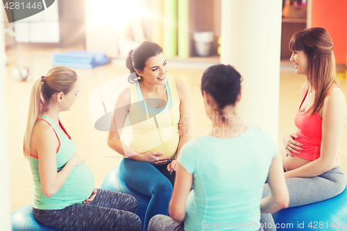 Image of happy pregnant women sitting on balls in gym