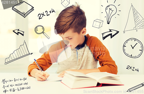 Image of student boy with book writing to notebook at home