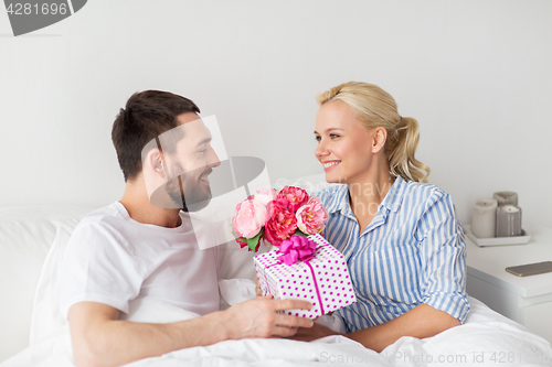 Image of happy couple with gift box in bed at home
