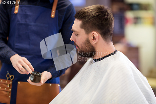 Image of barber showing hair styling wax to male customer