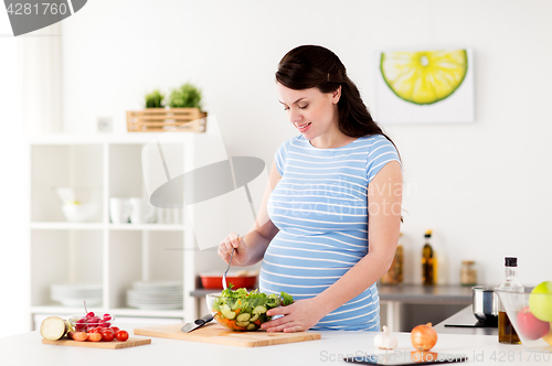 Image of pregnant woman cooking vegetable salad at home