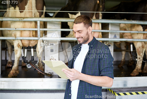 Image of man with clipboard and milking cows on dairy farm