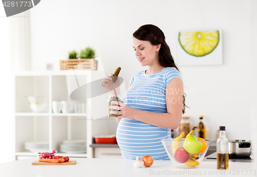 Image of pregnant woman eating pickles at home kitchen