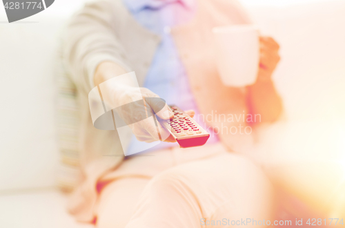 Image of senior woman watching tv and drinking tea at home