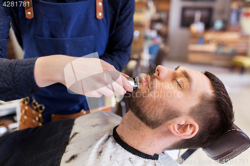 Image of man and barber with trimmer cutting beard at salon