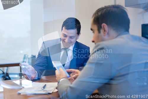 Image of Two young businessmen using smart phones and touchpad at meeting.