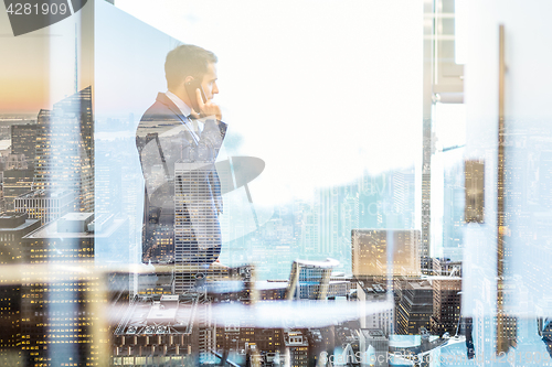 Image of Businessman talking on a mobile phone while looking through window in NY