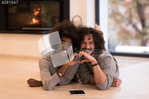 Image of multiethnic couple showing a heart with their hands on the floor