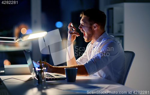 Image of angry businessman with smartphone at night office