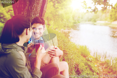 Image of happy couple with cups drinking in nature