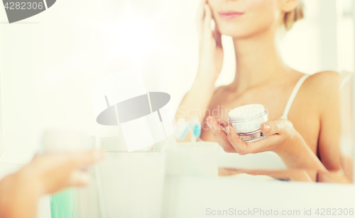 Image of close up of woman applying face cream at bathroom