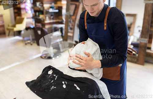 Image of barber softening clients face skin with hot towel