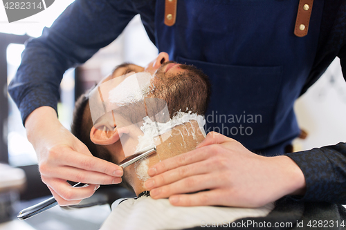 Image of man and barber with straight razor shaving beard