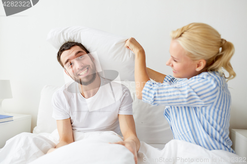 Image of happy couple having pillow fight in bed at home