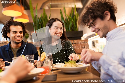 Image of happy friends eating and drinking at restaurant