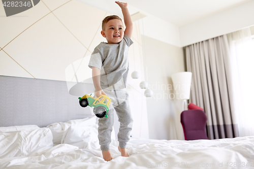 Image of happy little boy with toy car on home or hotel bed