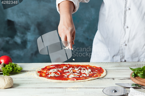 Image of Closeup hand of chef baker in white uniform making pizza at kitchen