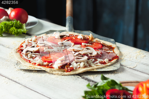 Image of Closeup of a home made raw pizza with cheese and tomato sauce on a wooden background