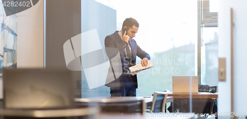 Image of Businessman talking on mobile phone while looking at wristwatch.