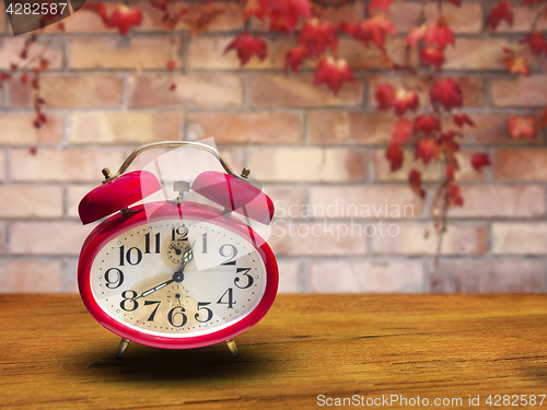 Image of Old red alarm clock on wooden table In front of the brick wall