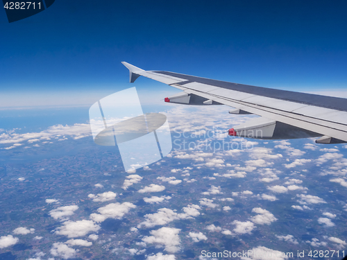 Image of View from a plane window: a plane wing over clouds and blue sky