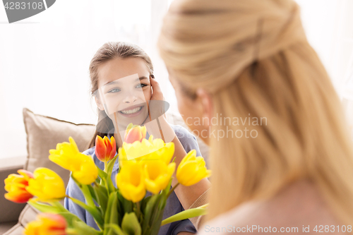 Image of happy girl giving flowers to mother at home