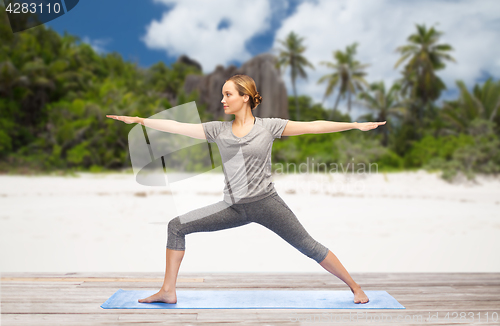 Image of woman doing yoga warrior pose on beach
