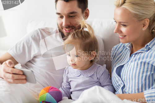 Image of happy family with smartphone in bed at home