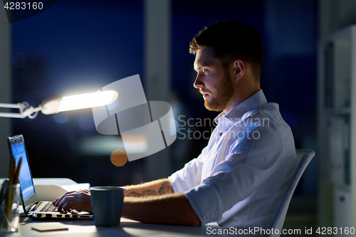 Image of man with laptop and coffee working at night office