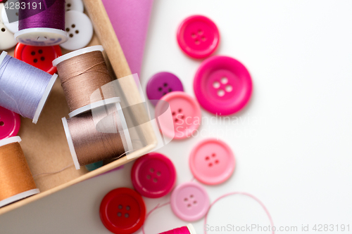 Image of box with thread spools and sewing buttons on table