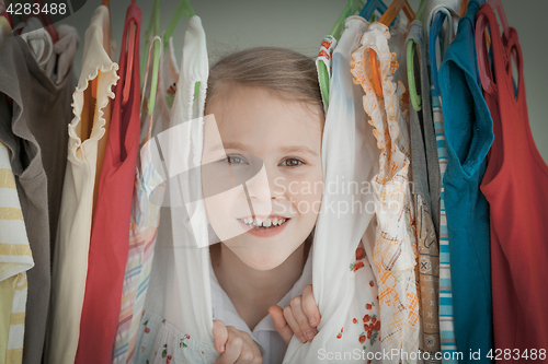 Image of portrait of a little girl standing near a hanger with clothes