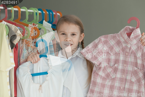 Image of portrait of a little girl standing near a hanger with clothes